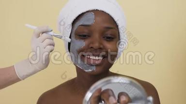 美容师用手在水疗沙龙里给年轻的非裔美国妇女<strong>敷面膜</strong>