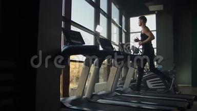 年轻的运动男女在运动健身房的跑步机上锻炼和跑步。 在大的全景窗户附近