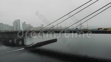 在市中心的工业烟雾中用钢缆连接的混凝土大桥。 一艘满载沙子的大驳船在宽阔的小溪下漂浮