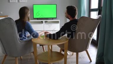 男人和女人坐在椅子上，用绿色的屏幕亲吻和看电视，用遥控器<strong>切换</strong>频道