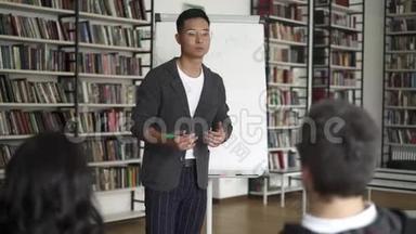 带着一张挂图在图书馆里讲课的亚洲年轻人