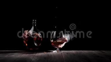 豪华白兰地。 穿着黑色衬衫的人把一个圆形瓶子放在靠近玻璃的木桌上，背景是黑色的干邑。