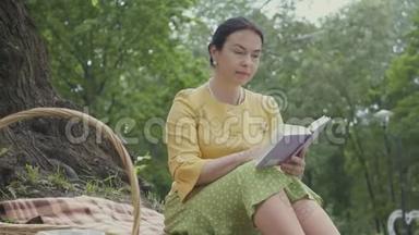 一位优雅美丽的成熟女人<strong>坐在</strong>公园<strong>树下</strong>的毯子上读这本书的肖像。 威克