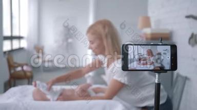 产妇护理，妈妈vlogger在手机上录制培训视频的同时教孩子如何换衣服。