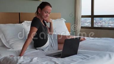 微笑着在网上约会的女人坐在床上拿着笔记本电脑