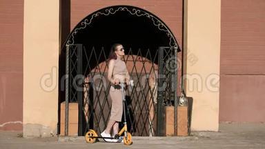 年轻漂亮的女人穿着裙子和太阳镜，在砖墙的背景上骑着一辆踢踏板车。 兵马俑