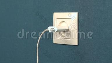 一个男人把电话充电器插入墙上的插座。 墙上的罗塞特和深蓝色壁纸。 特写