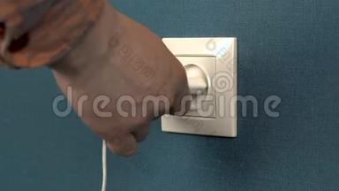 一个男人从墙上的插座里掏出一个电话充电器。 墙上的罗塞特和深蓝色壁纸。 特写
