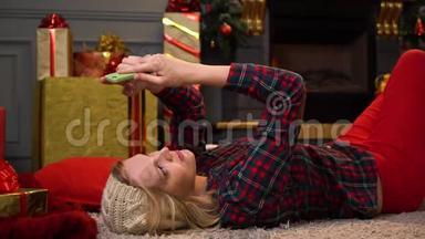 年轻漂亮的女孩或女人穿着红色格子衬衫躺在地板上，拿着<strong>圣诞树</strong>通过电话进行<strong>视频</strong>通话