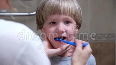 特写母亲早上帮助她的小儿子清洁牙齿。 女人帮儿子刷牙。