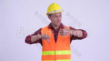 年轻迷茫的西班牙男子建筑工人在竖起大拇指和竖起大拇指之间做出选择