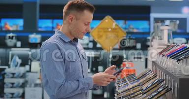 年轻的帅哥穿着蓝色衬衫，在一家电子商店里选择了一部新手机。 现代技术<strong>采购</strong>