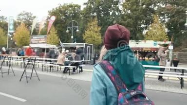 慢动作年轻的白种人女游客穿着蓝色夹克和背包在城市集市上走来走去。 反对