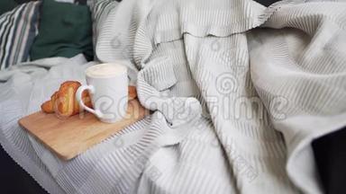静态新鲜咖啡和一个热牛角面包在一个<strong>大沙发</strong>与枕头，毛毯和格子。 Hygge或Lagom