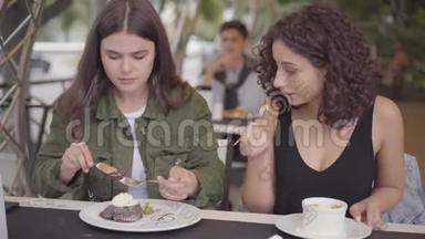 两个女朋友坐在户外咖啡馆吃蛋糕的肖像。 年轻女孩一起<strong>享用美食</strong>，一起分享