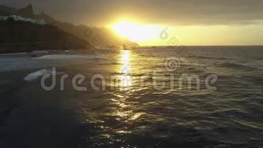 在美丽的日落光线下，在加那利群岛的特内里费附近的贝尼霍海滩上鸟瞰海浪。 冲浪者在游泳