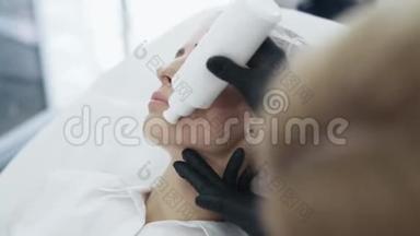 手套中美容师的慢动作特写双手在治疗前在病人脸上涂上特殊的凝胶