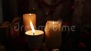 圣诞节的温暖：三支点燃的蜡烛，一支在前景中有着巨大的火焰，红色和金色的球，脱钩的球，缎子