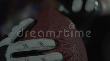 职业运动员双手特写，戴运动手套，手持橄榄球。