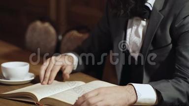 一个男人的特写`手拿着一本打开的纸<strong>书</strong>，用手指<strong>翻页</strong>，喝茶。 男人`手