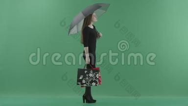 穿着黑色小裙子的漂亮女人正站在一把带购物袋的伞下。 她站在一边