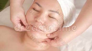 美容院中年亚洲妇女面部按摩。 特写镜头。 美容师双手`手指的移动