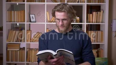 在大学里，一位有魅力的男大学生正在看书，看着摄像机，开心地笑着