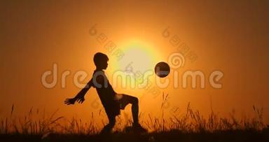 小男孩足球运动员剪影，用球练习，夕阳红黄金时刻，慢动作..