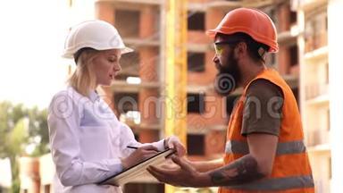 戴防护头盔的建筑工人在施工现场讨论。 施工现场的施工人员.. 两个工程师