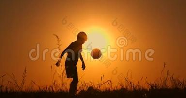 小男孩足球运动员剪影，用球练习，夕阳红黄金时刻，慢动作..