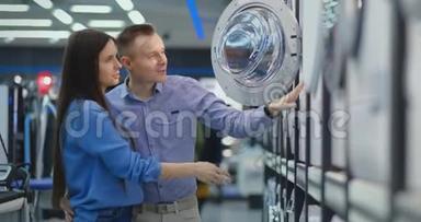 美丽的男人和女人选择现代<strong>智能洗衣机</strong>在消费电子商店为他们的新的现代家居。