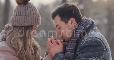 在一个白雪覆盖的公园里，一个有爱心的男人在冬天温暖`妻子的双手。