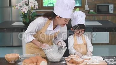 漂亮的女人和可爱的亚洲小男孩戴着眼镜，戴着厨师帽，围着围裙在家里的厨房里玩耍和烤面包。霍姆