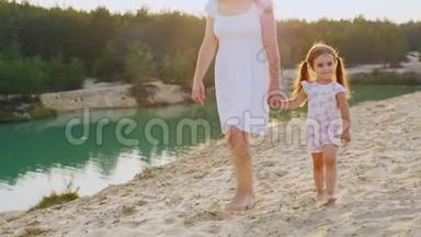 母亲和女儿在美丽的湖水边散步，妈妈是一个女孩`的手臂