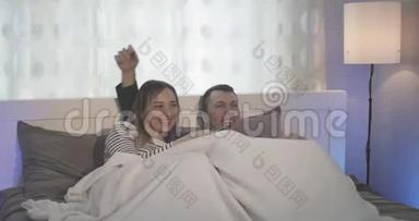 快乐的女人和男人躺在床上看电视。