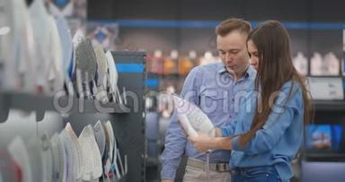 年轻的已婚夫妇选择在电器商店的一个新家买熨斗。 一个女人握着她的手，看着