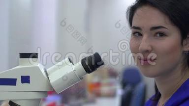年轻漂亮的女人在实验室用显微镜近距离做分析。 那位女士微笑着看着镜头