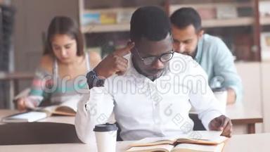 非裔<strong>美国</strong>男大学生戴着眼镜在<strong>图书馆</strong>准备考试，读着一本书