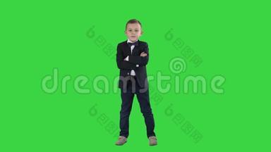 小男孩穿着正式服装在绿色屏幕上交叉双手，彩色钥匙。