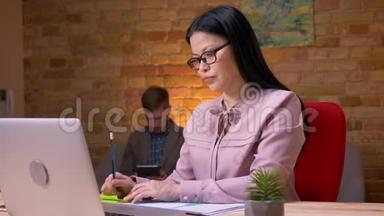 亚洲成年女商人的特写镜头，她在笔记本电脑上工作，为坐在电脑前的商人处理图表