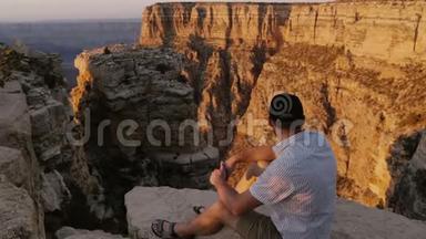 大峡谷上，坐在大岩石上观看日落景色的年轻游客正在观看高角度摄像机