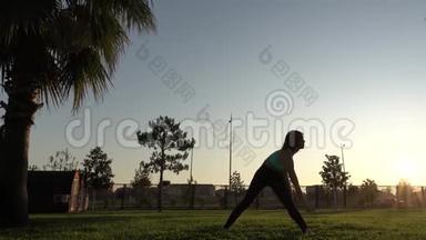 一个年轻漂亮的女孩在棕榈树上做瑜伽。 慢动作4k。 剪影