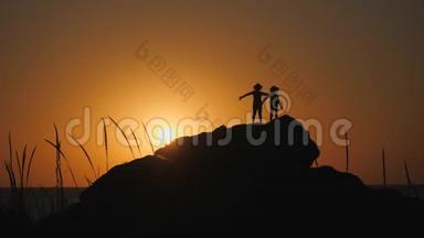 孩子们在夕阳下剪影。 戴<strong>帽檐</strong>的男孩站在岩石上。 石头躺在海边