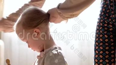 母亲给女儿梳头。一个女人早上正在给她可爱的女儿梳头。妈妈做她的小发型