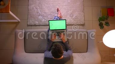 在舒适的家中，坐在沙<strong>发</strong>上的年轻人用绿色屏幕在笔记本电脑上<strong>发信息</strong>的特写镜头