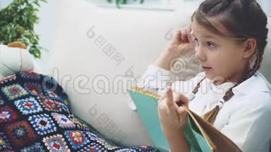 可爱的小女孩坐着，双腿蜷曲，为她的泰迪读童话故事，有感情地移动她的手，表现出