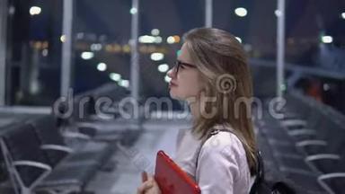 一个年轻、美丽、微笑的女孩手里拿着一台笔记本电脑和一个公文包，沿着机场<strong>空无</strong>一人的候机楼走着