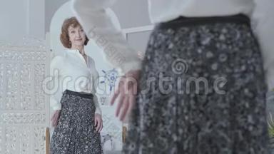 可爱优雅的老女人看着镜子，审视着她的倒影。 那位女士看着她穿着新长裙