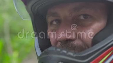 近距离<strong>面对</strong>骑摩托车的男子，戴着摩托头盔，看着相机和<strong>微笑</strong>。 戴着防护帽的莫托摩托车手