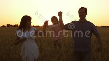 快乐的女儿和爸爸妈妈一起周游一片成熟的小麦，孩子笑了。 家庭团队合作。 宝贝